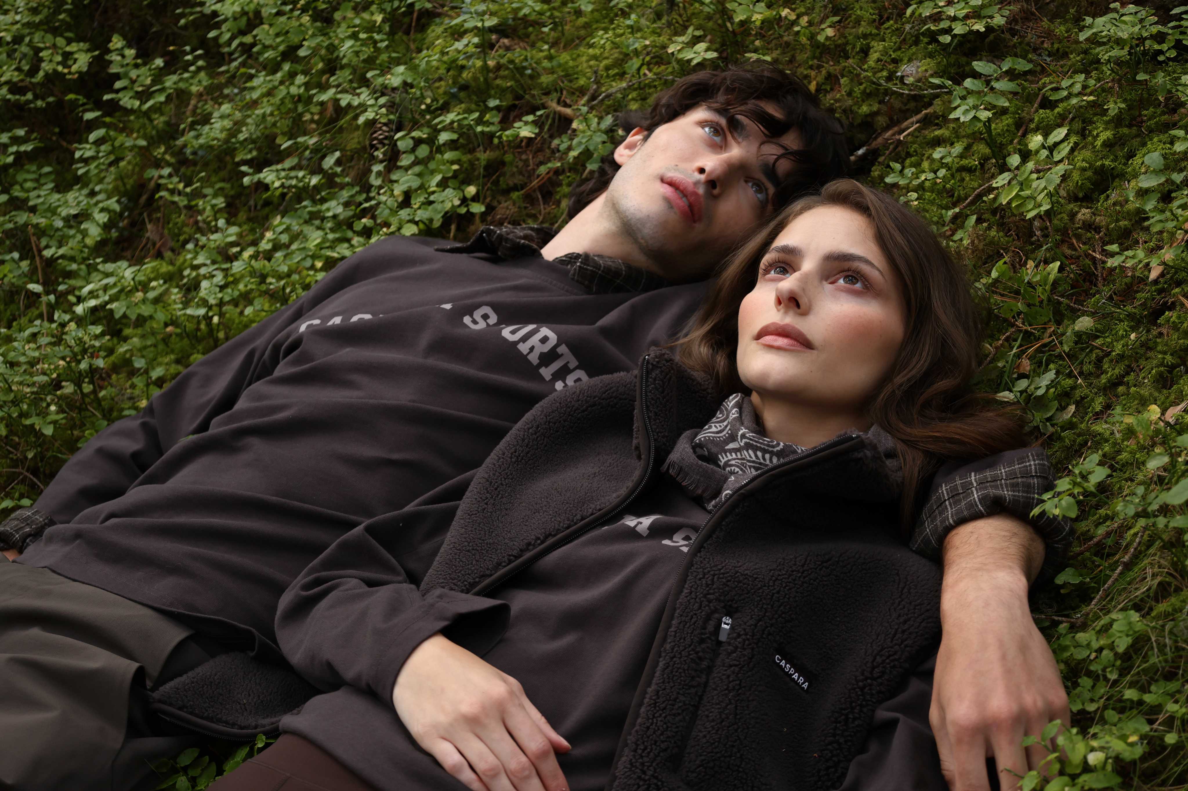 Man and woman lying on mossy ground wearing espresso CASPARA CS Signature long sleeve shirts.